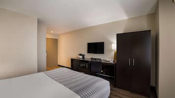 Una habitación de hotel con cama, escritorio, silla, televisor y armario.