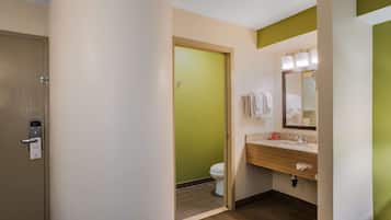 Een hotelbadkamer met een groene deur, een wit toilet, een wastafel met spiegel en een handdoekrek.
