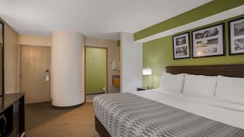 Habitación de hotel con cama, escritorio, silla, lámpara y un muro con fotografías enmarcadas.