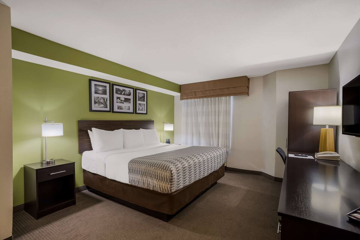 A hotel room with a bed, bedside table, lamp, and a desk with a chair.