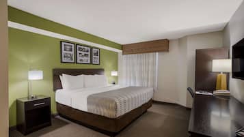 A hotel room with a bed, bedside table, lamp, and a desk with a chair.