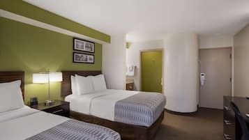 A hotel room with two beds, a nightstand with a lamp, a dresser, and a door leading to a bathroom.