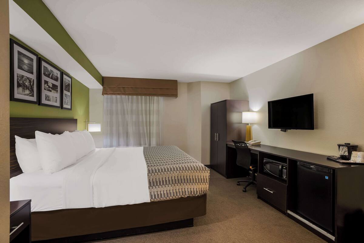 A hotel room with a bed, a desk with a computer, a television, and a minibar.