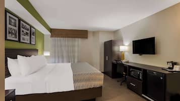 Una habitación de hotel con cama, escritorio con computadora, televisión y minibar.