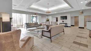 A spacious lobby with a high ceiling, a seating area with sofas and chairs, a reception desk, and a television screen.