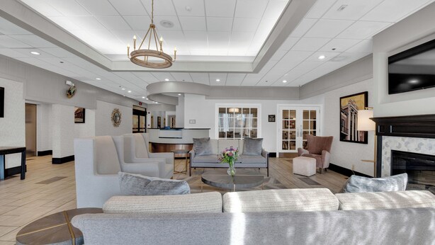 A spacious living room with a large sectional sofa, a coffee table, and a fireplace. There is a television mounted on the wall and a chandelier hanging from the ceiling.