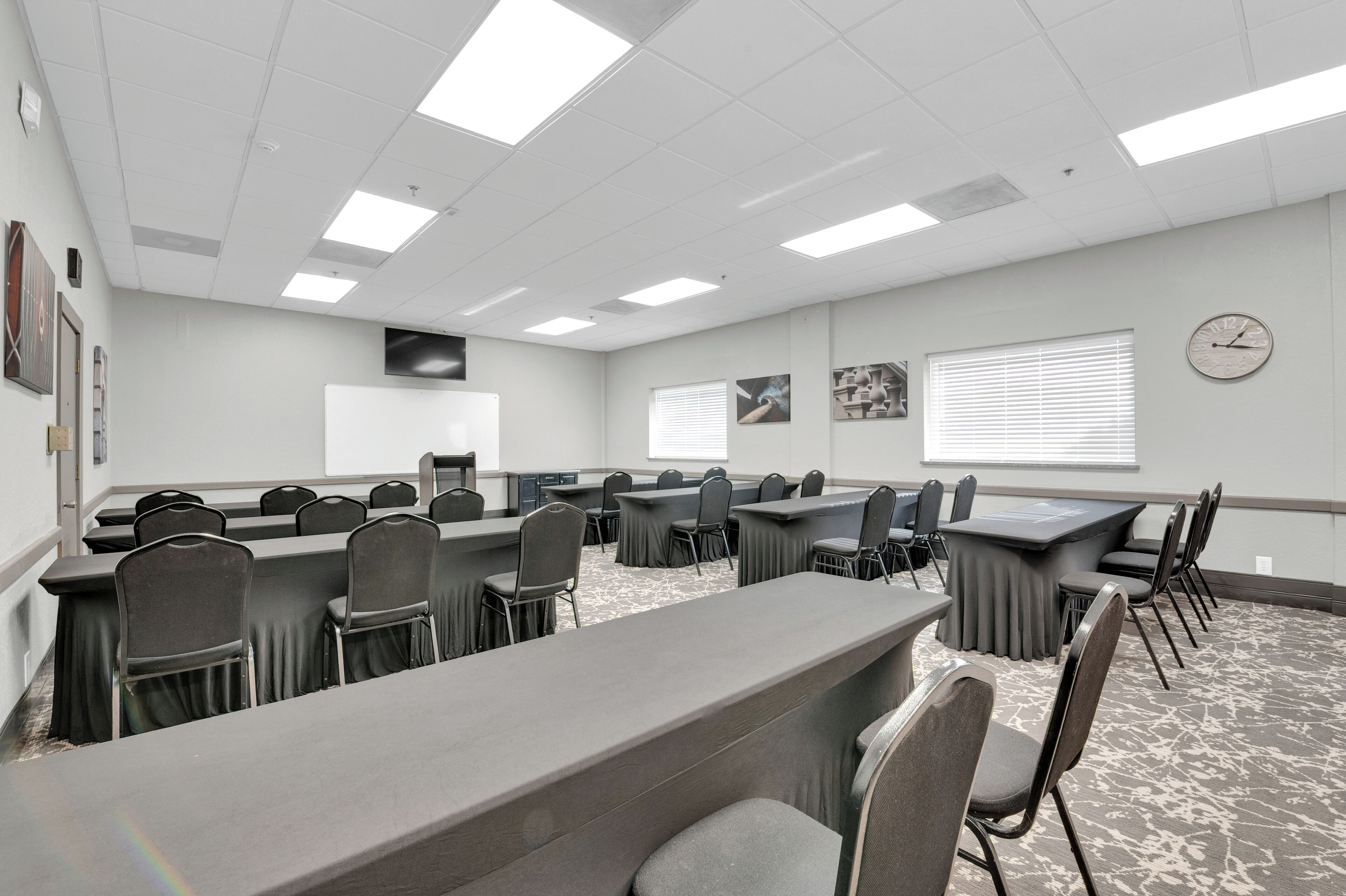 A conference room with long tables and chairs, a clock on the wall, and a projector screen.