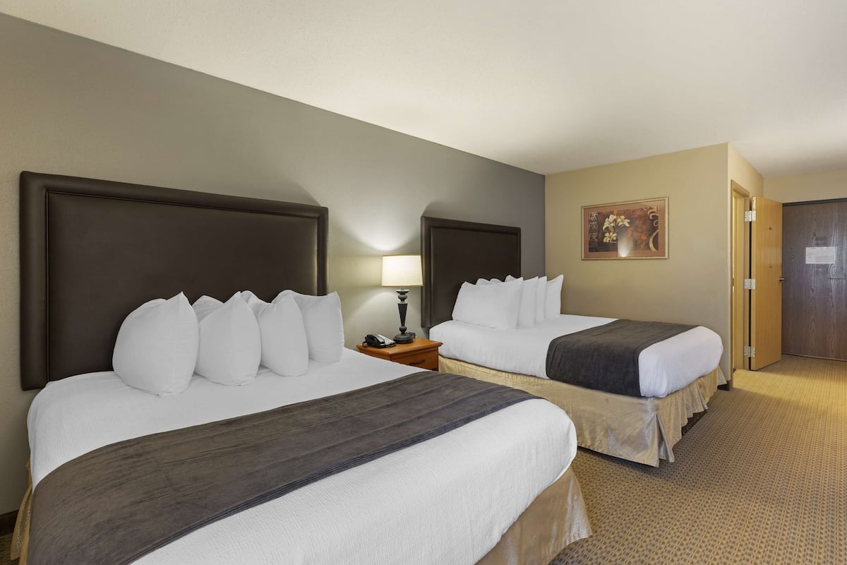 A hotel room with two beds, a nightstand with a lamp, and a door.