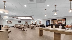 A spacious room with multiple tables and chairs, a reception desk, and a counter with various items.