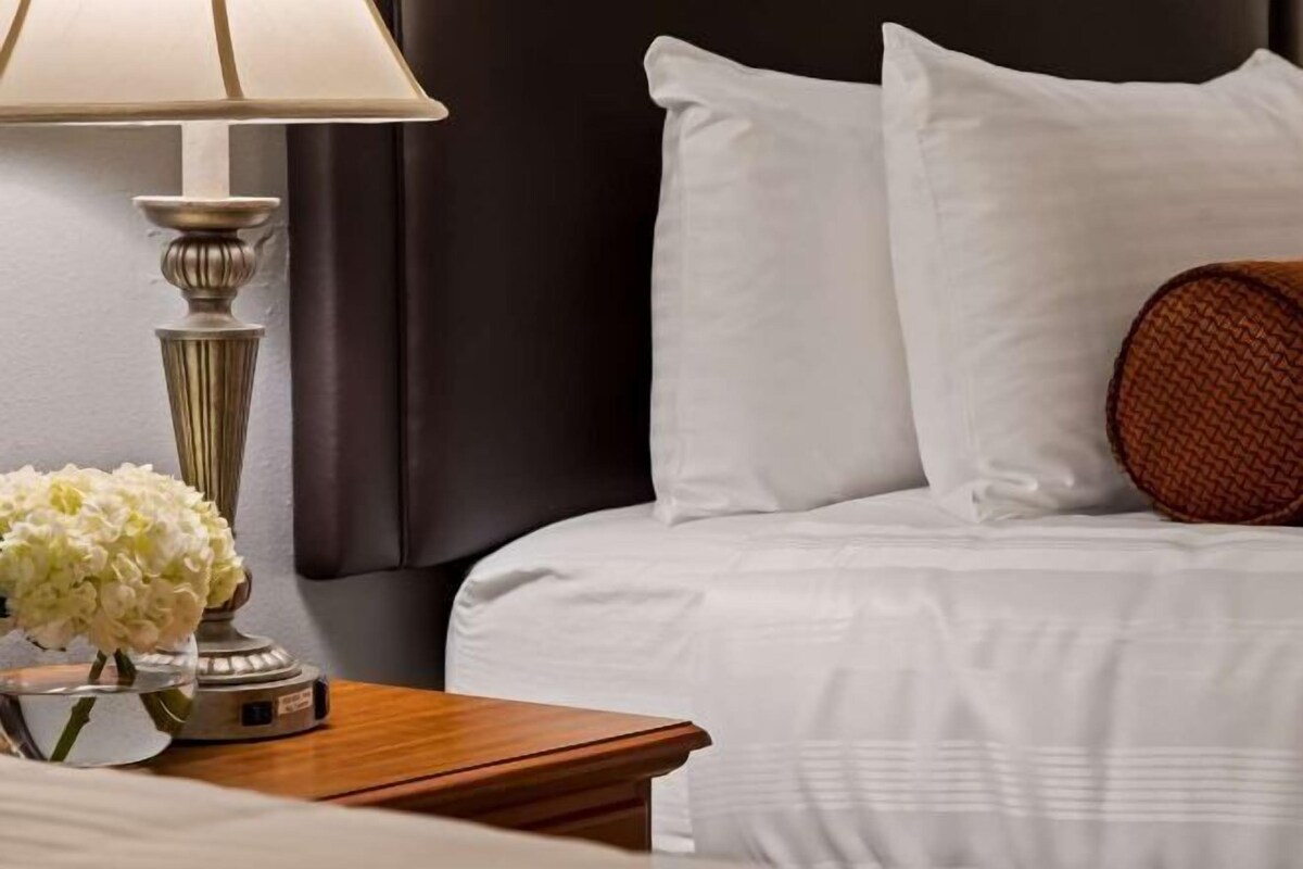 A hotel room with a bed, a nightstand, a lamp, and a vase with flowers.