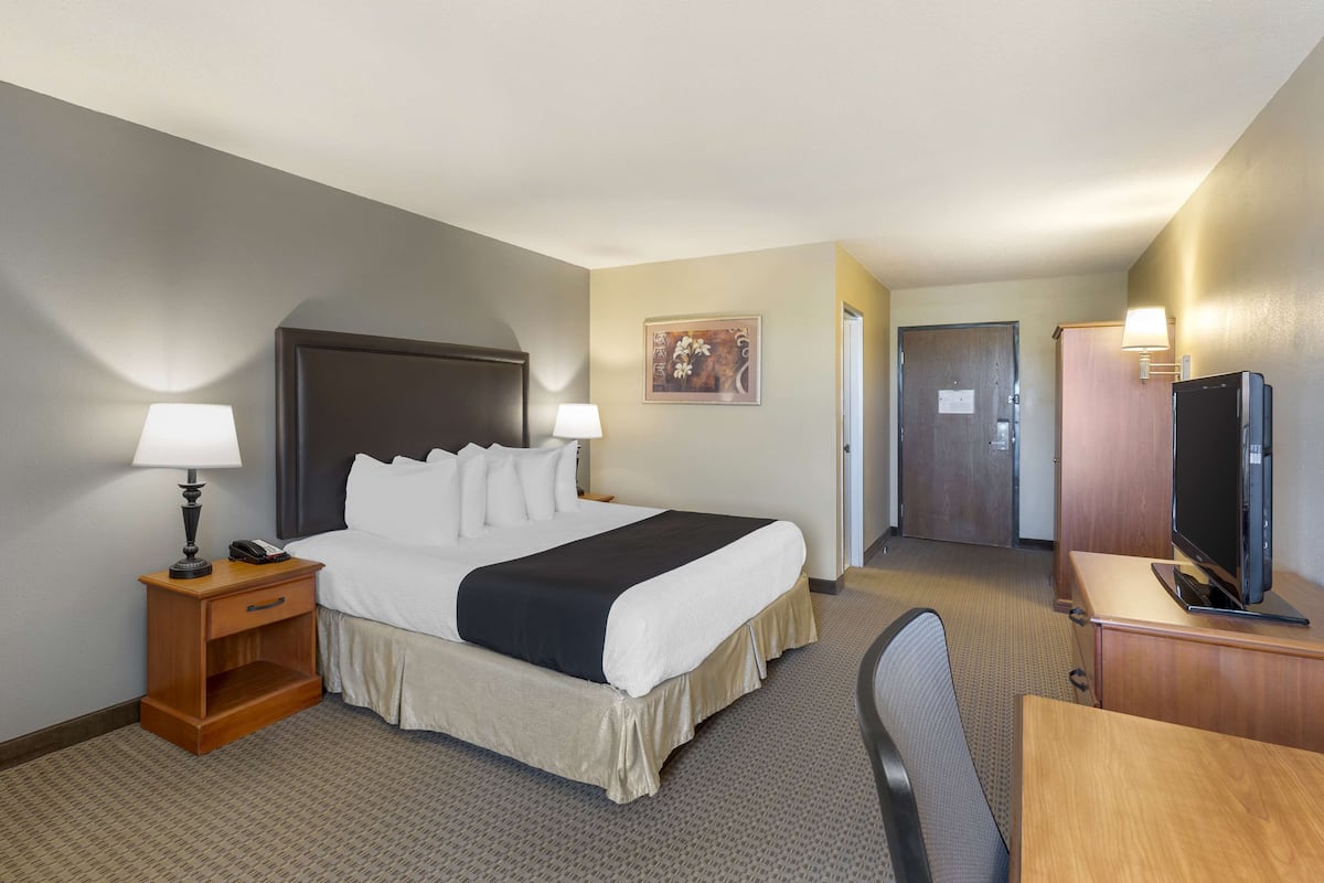 A hotel room with a bed, bedside lamps, a desk with a television, and a door leading to another room.