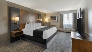 A hotel room with a large bed, bedside tables with lamps, a flat-screen TV, and a large window with curtains.