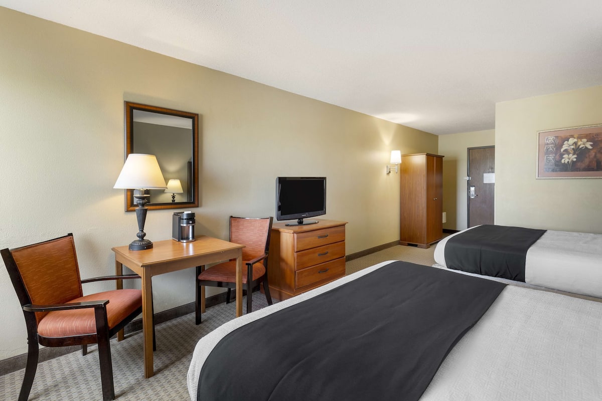 A hotel room with two beds, a desk with a lamp, a television, a dresser, and a chair.