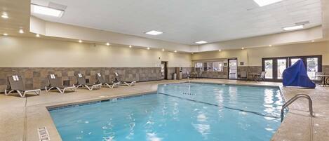 An indoor swimming pool with multiple lanes, lounge chairs, and a covered seating area.