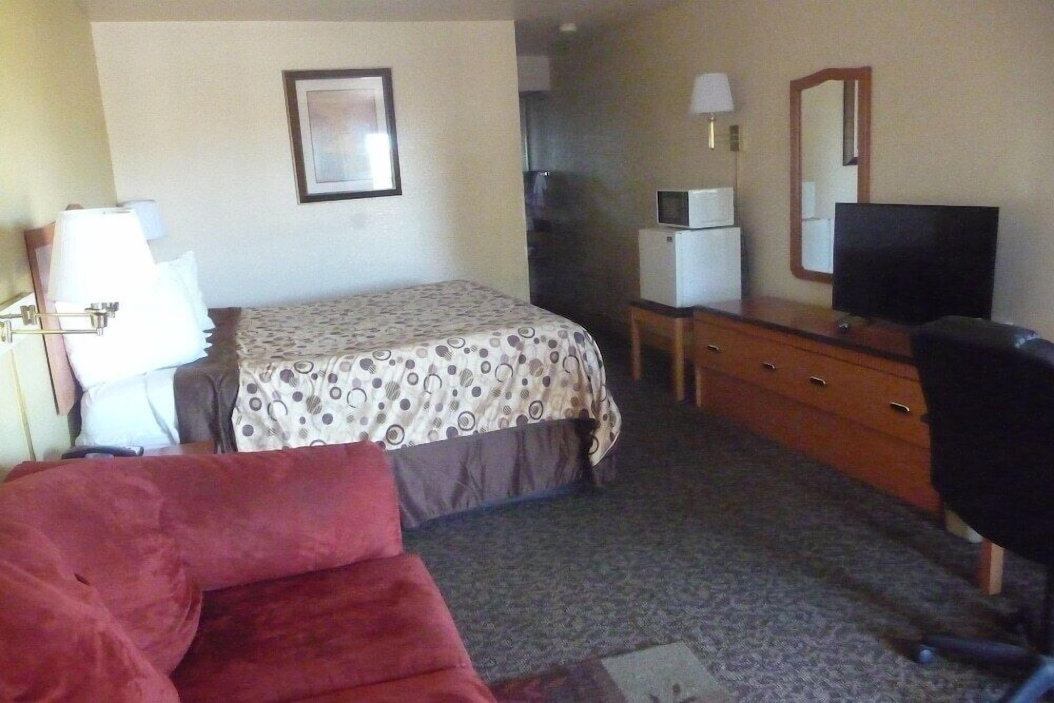 A hotel room with a bed, a desk with a computer, a television, and a red chair.