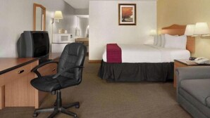 A hotel room with a bed, a desk with a computer, a chair, a couch, and a microwave in the background.