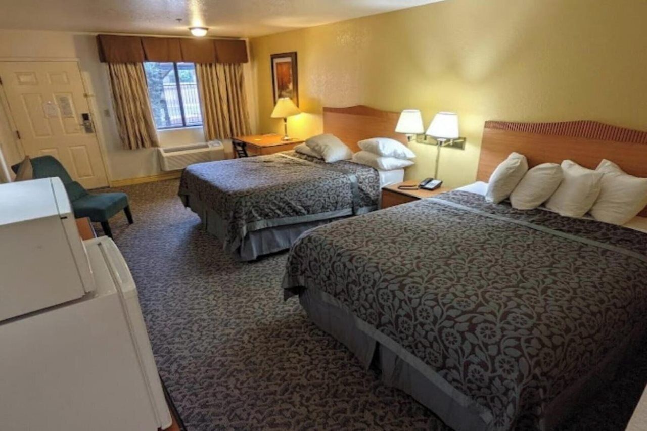 A hotel room with two beds, a desk, a chair, and a window with curtains.