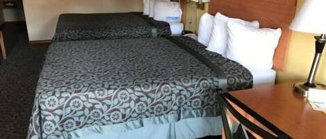 A hotel room with two beds, a wooden headboard, a desk with a chair, and two lamps.