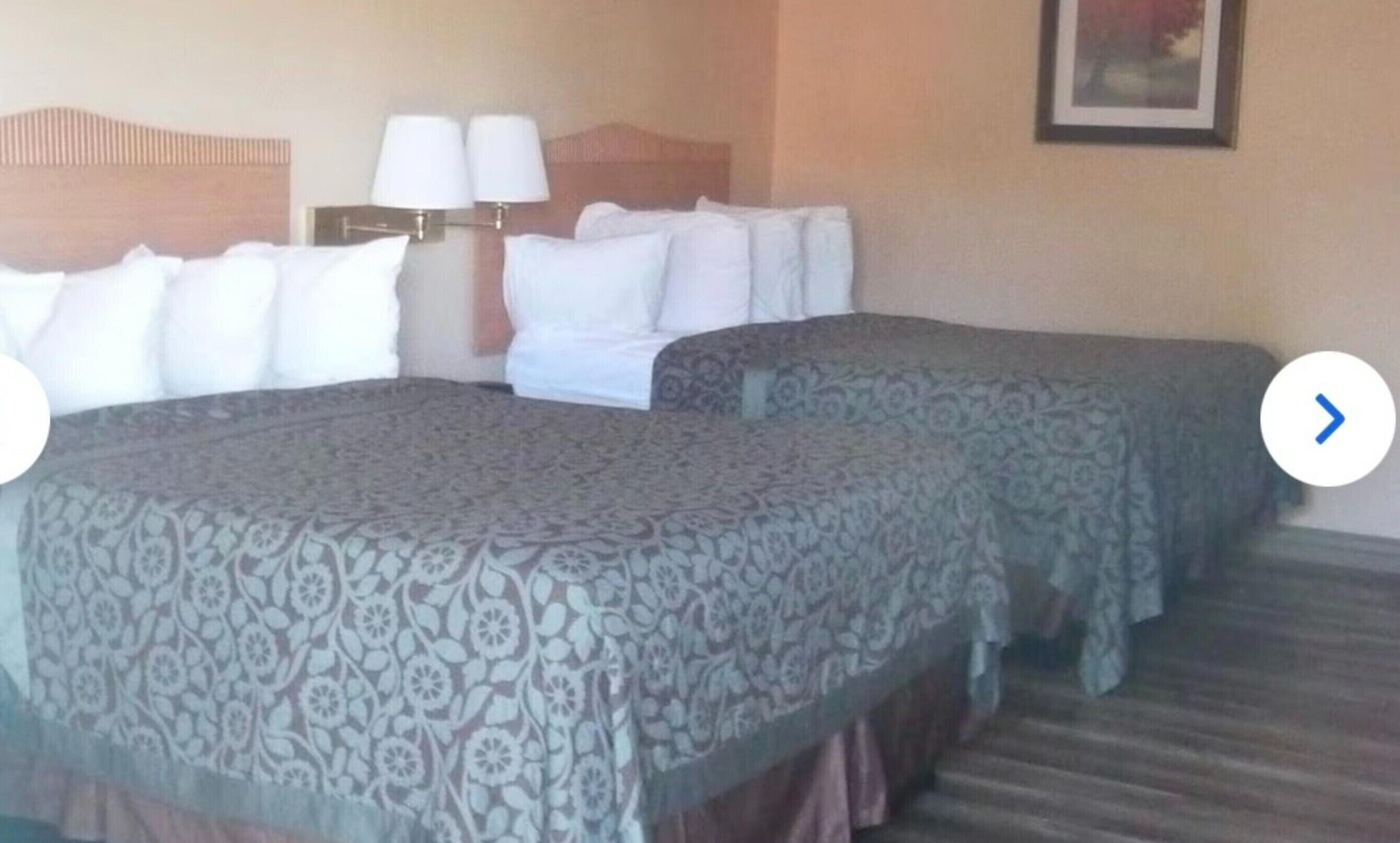 Una habitación de hotel con dos camas, un cabecero con lámparas y un cuadro en la pared.