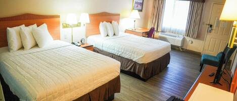 A hotel room with two beds, a desk, a chair, a lamp, and a window with curtains.