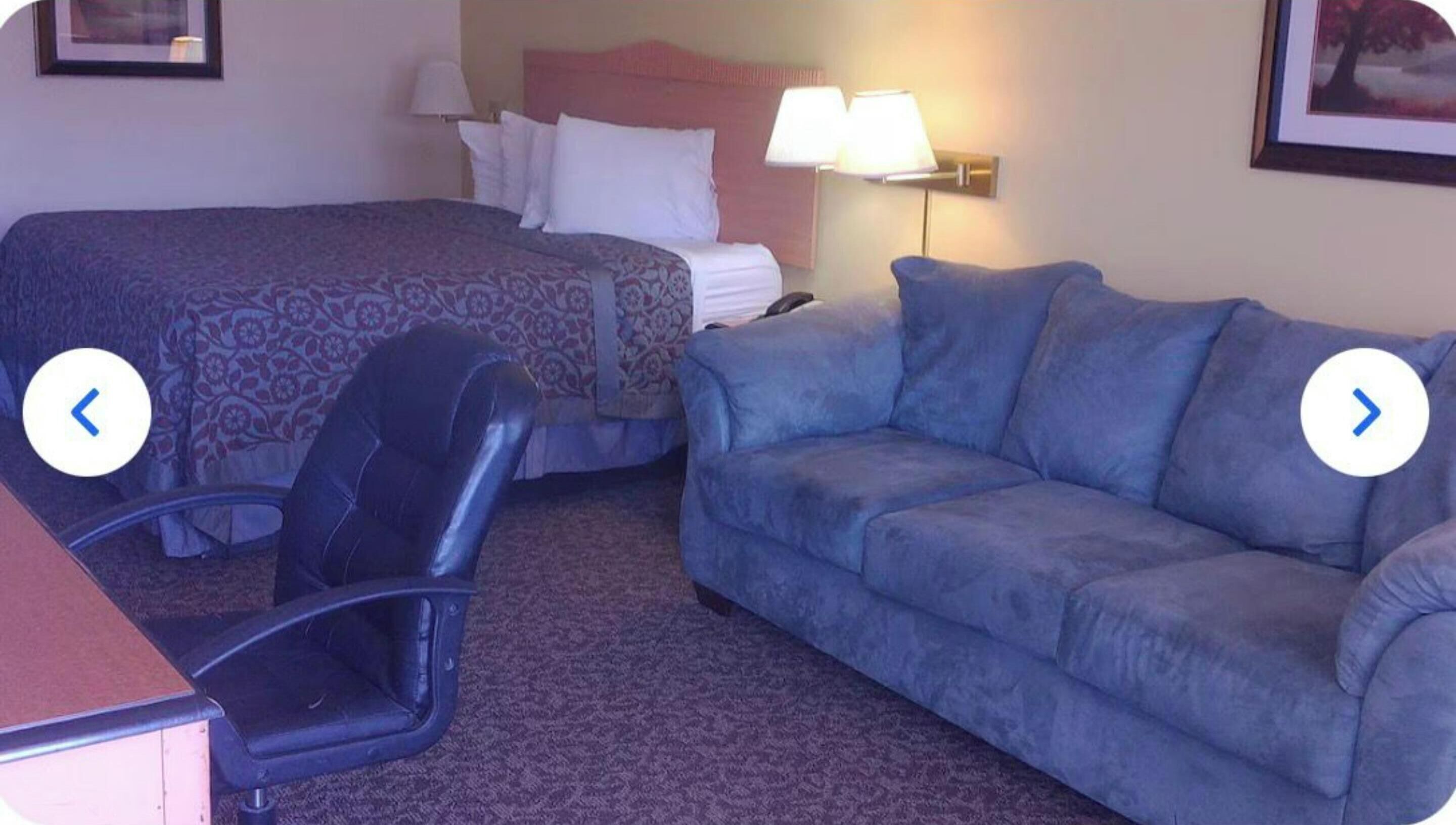 A hotel room with a bed, a blue sofa, a chair, and a desk.