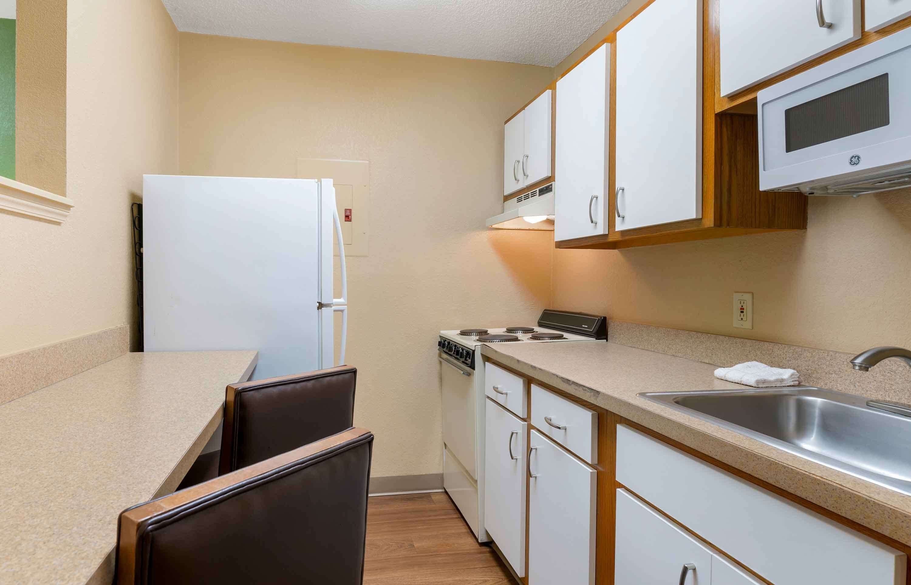 Una cocina compacta con alacenas blancas, estufa, lavamanos y refrigerador.
