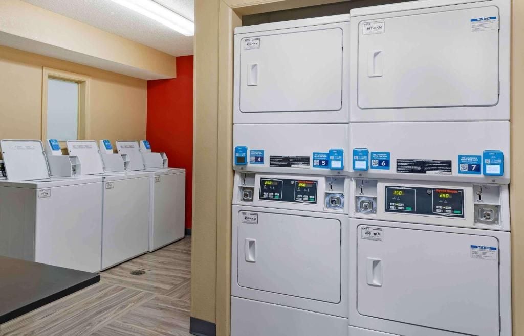 A laundry facility with multiple washing machines and dryers, each with control panels and labels.