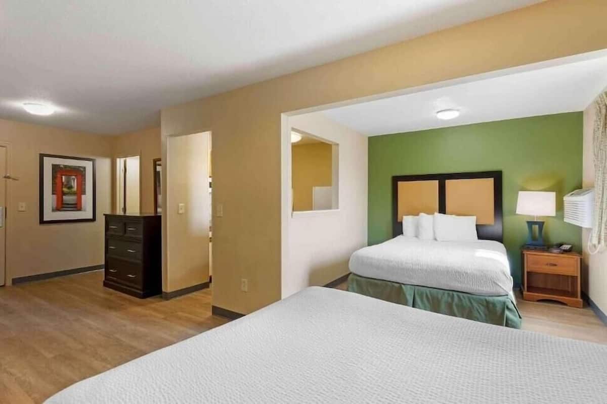 Una habitación de hotel con una cama grande, un tocador, una mesita de noche y una pared de acento verde.