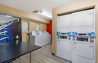 A laundry room with multiple washing machines and dryers, a drying rack, and a control panel with buttons and a display.