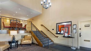 A hotel lobby with a staircase, a reception desk, and a seating area with chairs and a table. - Studio 6 Extended Stay - St Louis, MO - Westport/Craig Road (Maryland Heights)
