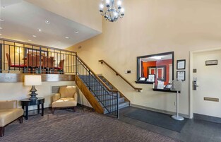A hotel lobby with a staircase, a reception desk, and a seating area with chairs and a table.