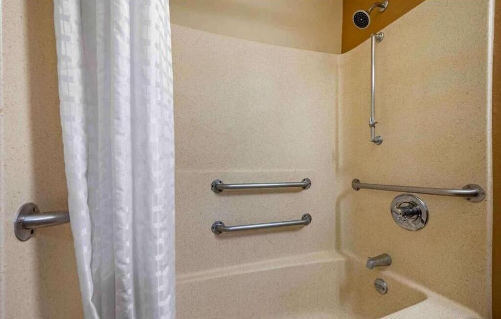 Un baño con ducha, barras de apoyo y un perchero para toallas.