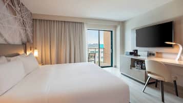 A hotel room with a large bed, a desk with a chair, a flat-screen TV, and a balcony with a view.