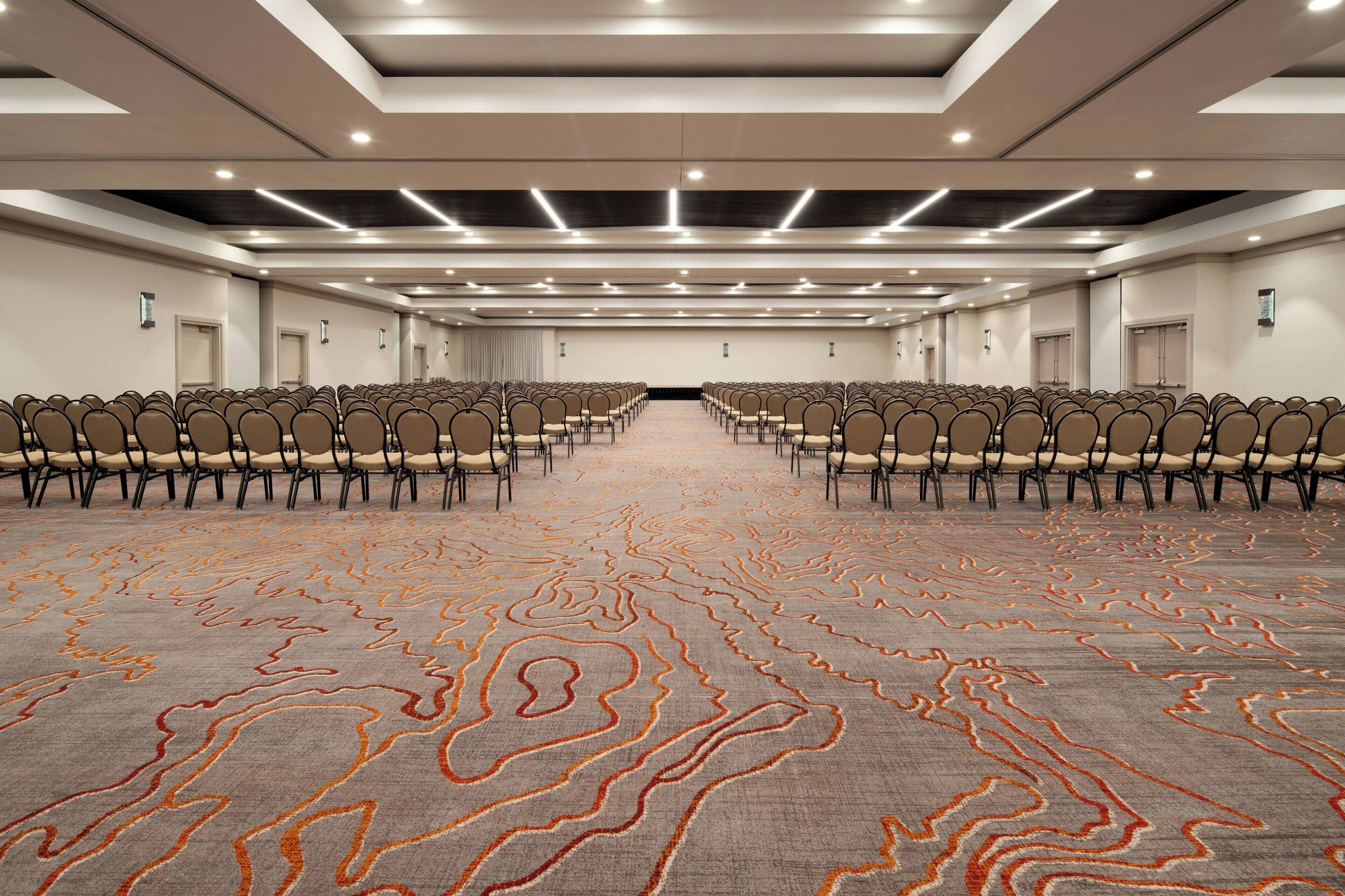 Une grande salle de conférence avec des rangées de chaises, une moquette à motifs et un design moderne au plafond.