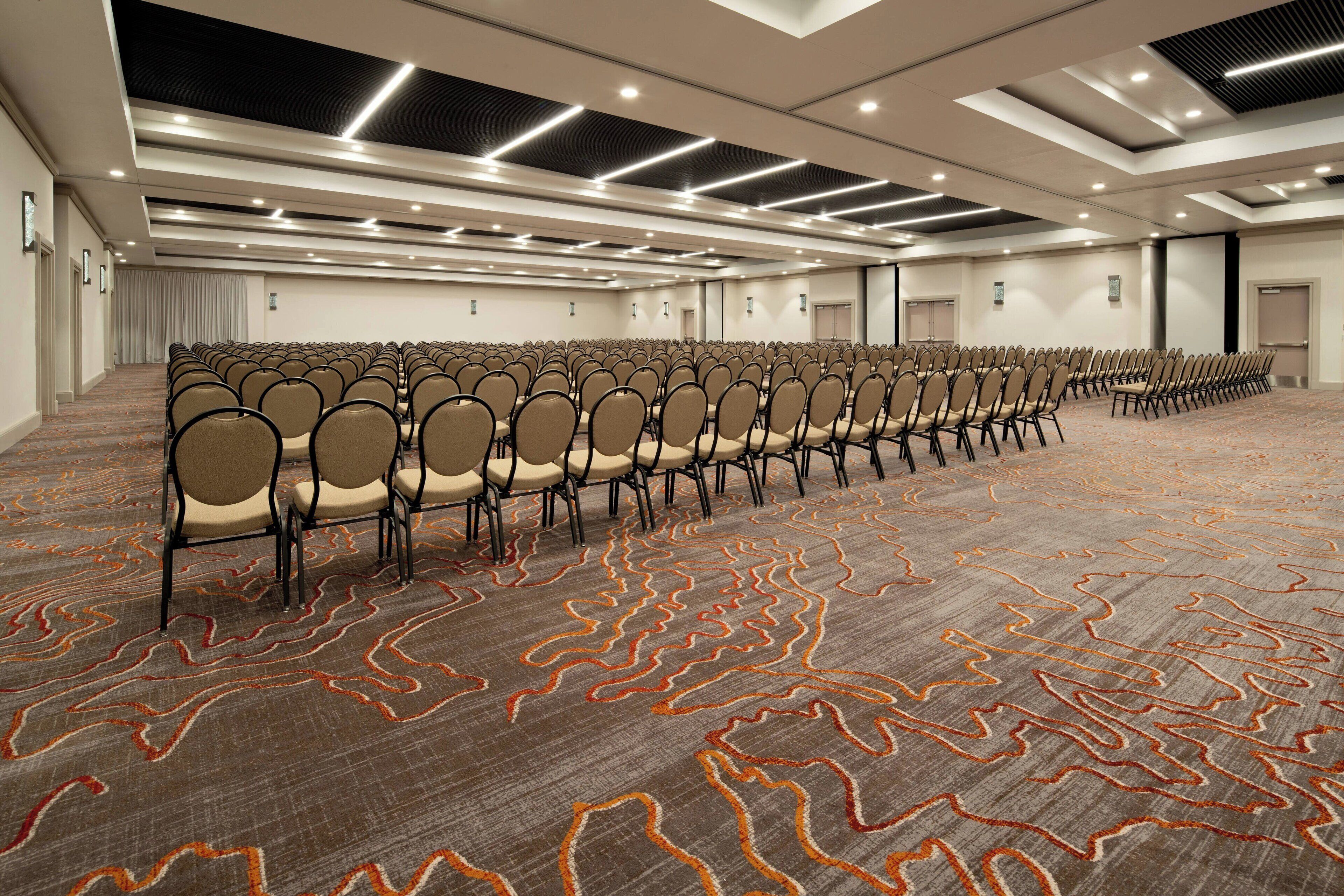 A large conference room with rows of chairs, carpeted floor, and modern lighting fixtures.