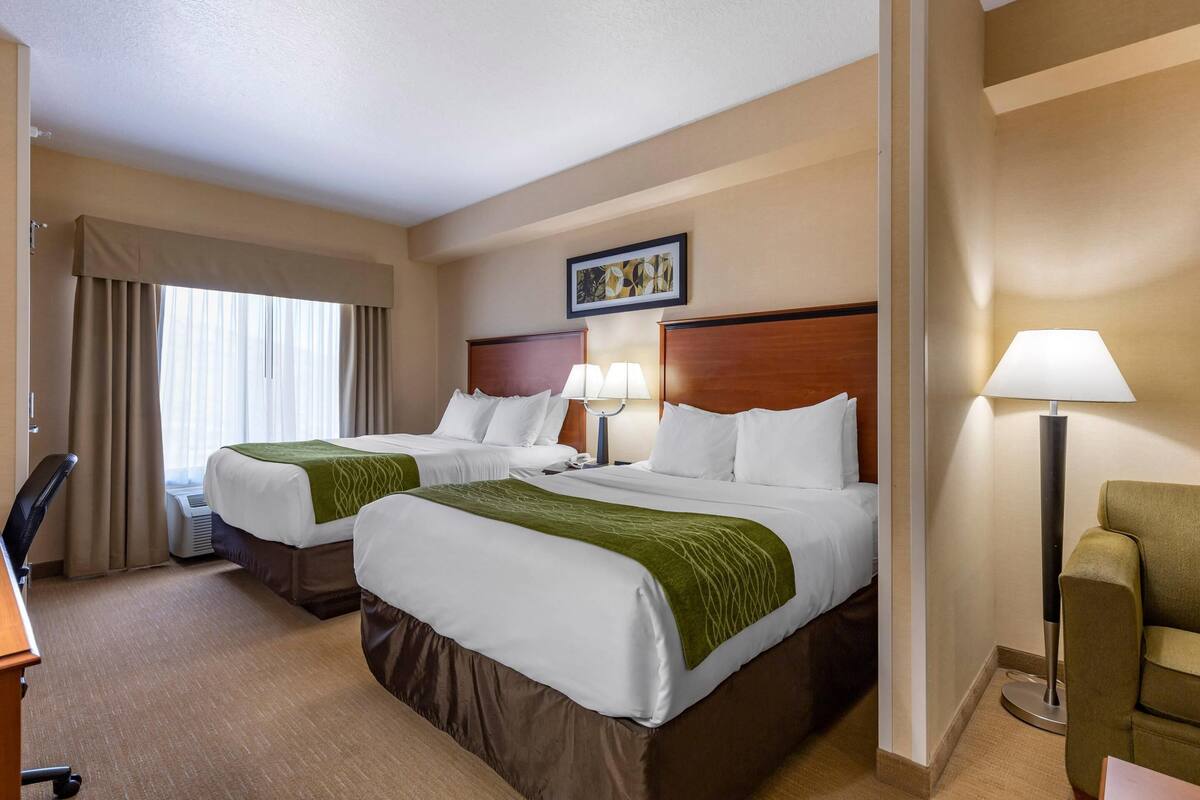 A hotel room with two beds, a desk, a chair, a lamp, and a picture on the wall.