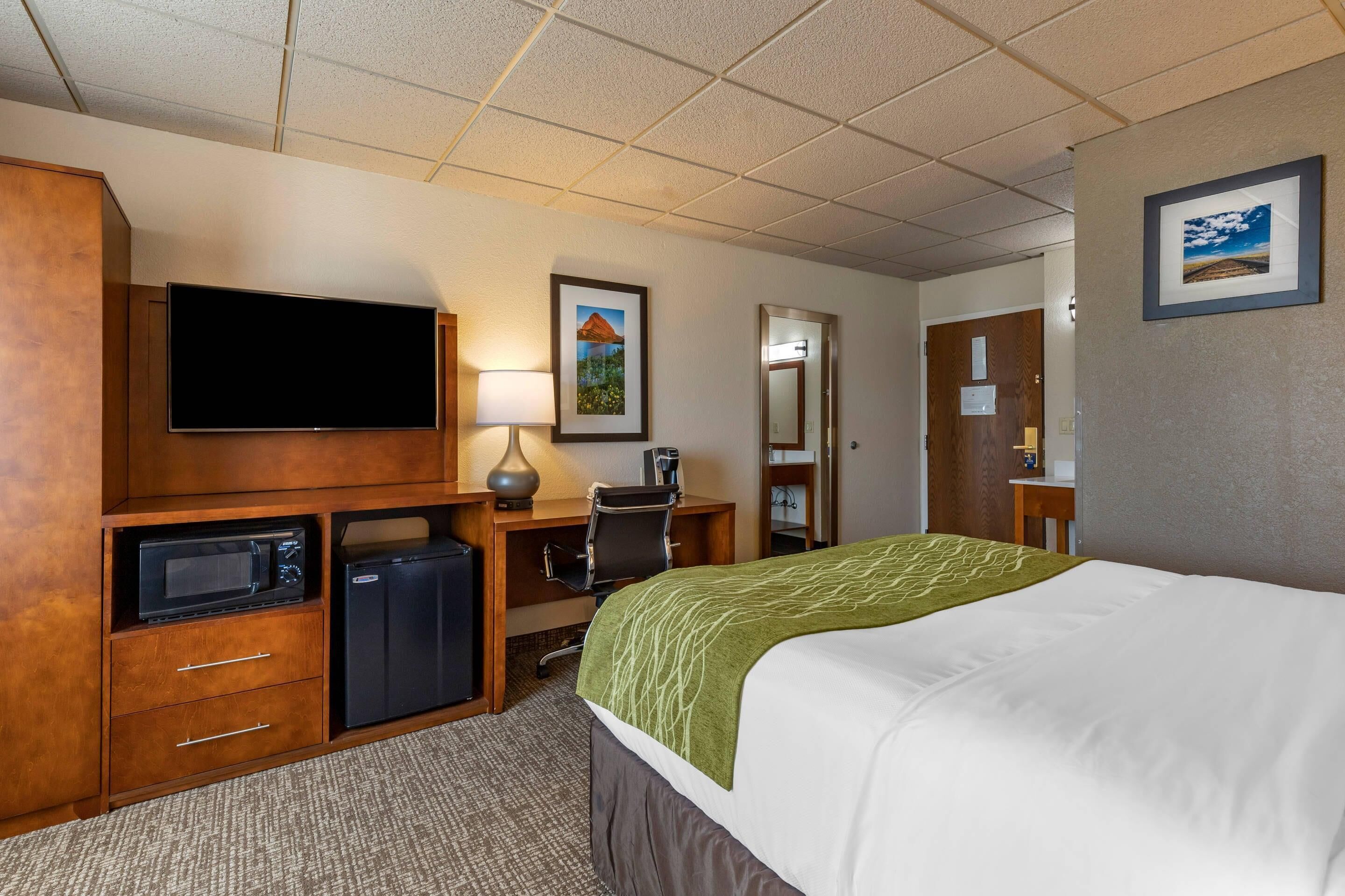 A hotel room with a bed, a television, a desk with a computer, a microwave, and a refrigerator.