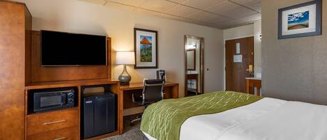 A hotel room with a bed, a television, a desk with a computer, a microwave, and a refrigerator.