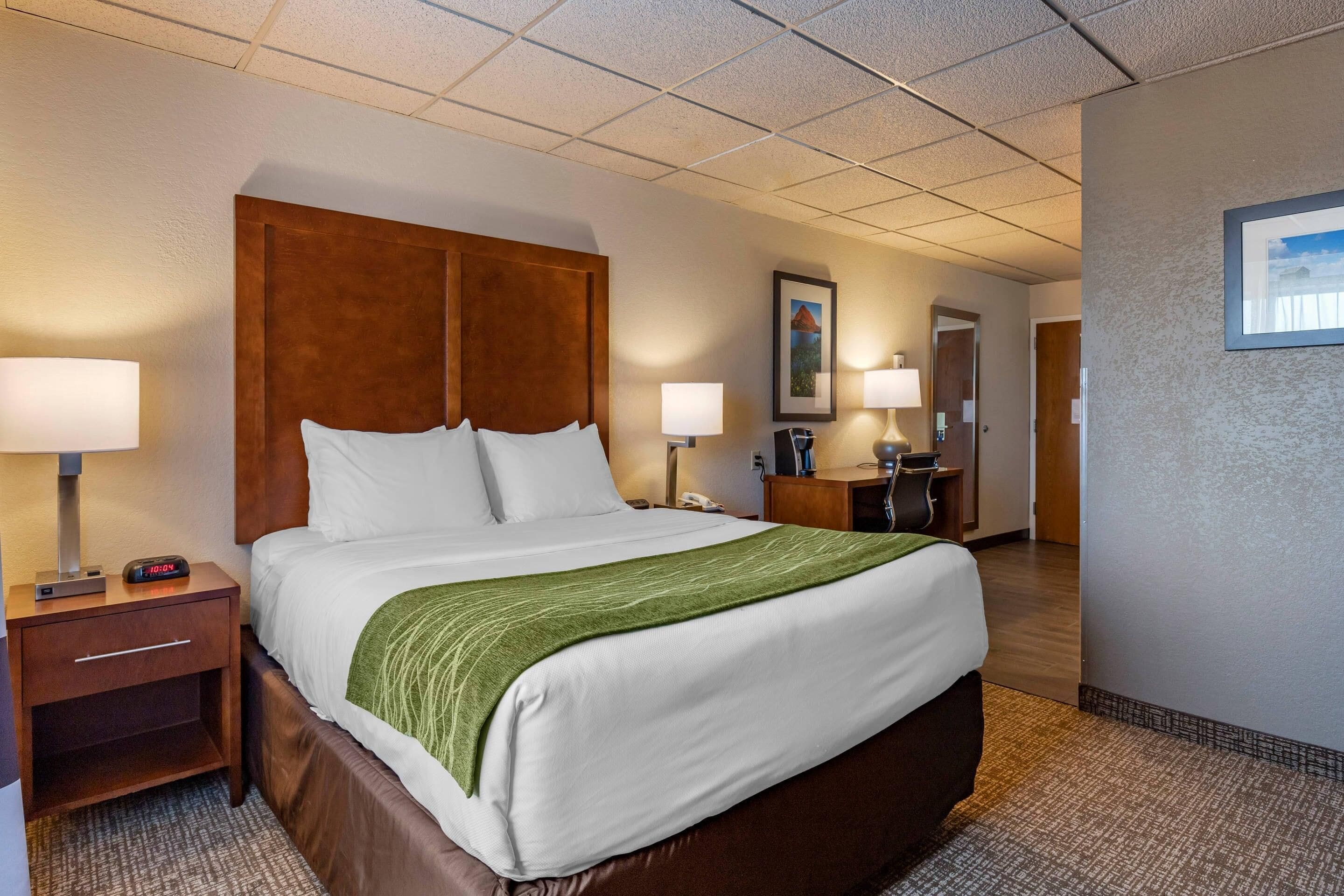 A hotel room with a large bed, two bedside tables, a nightstand, a desk, and a chair.