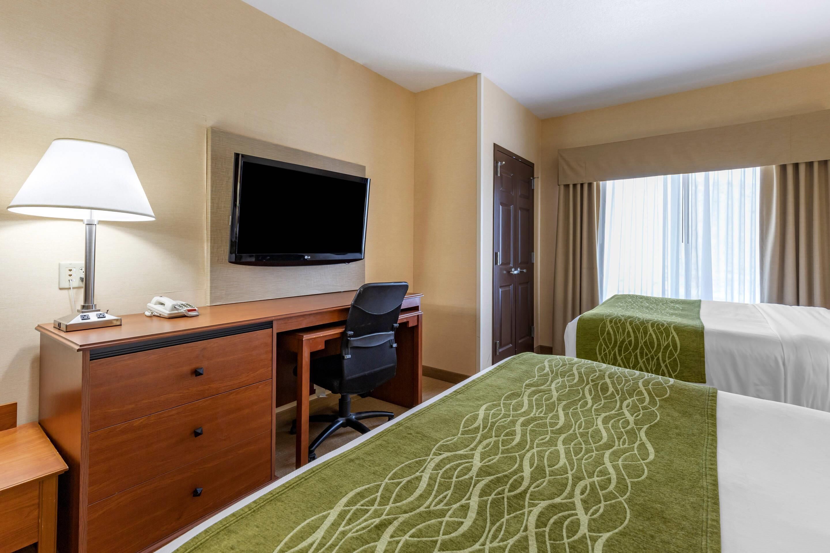 A hotel room with a desk, chair, television, two beds, and a window with curtains.