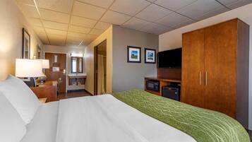A hotel room with a bed, a desk with a lamp, a television, a wardrobe, and a bathroom visible through an open door.