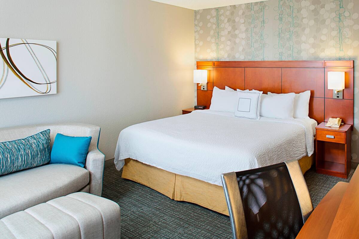 Quarto de hotel com uma cama grande, um sofá, uma poltrona e uma escrivaninha.