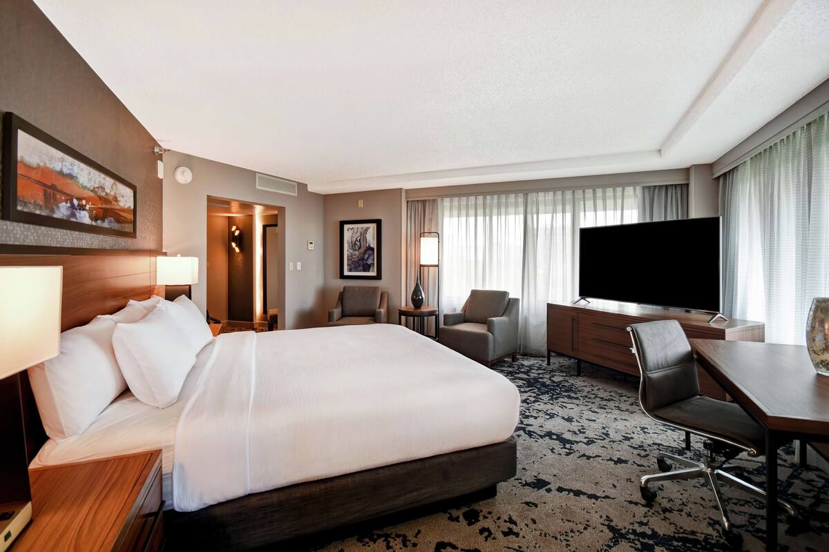 A hotel room with a large bed, a desk with a chair, a TV, and a painting on the wall.