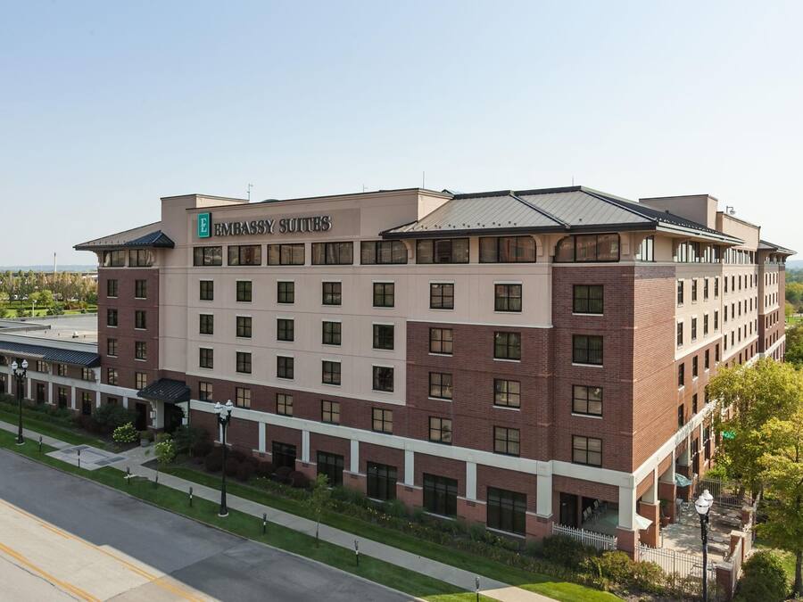 Un hotel de varios pisos con un llamativo letrero 'Embassy Suites', que presenta una combinación de fachadas de ladrillo y color beige, y un techo plano.