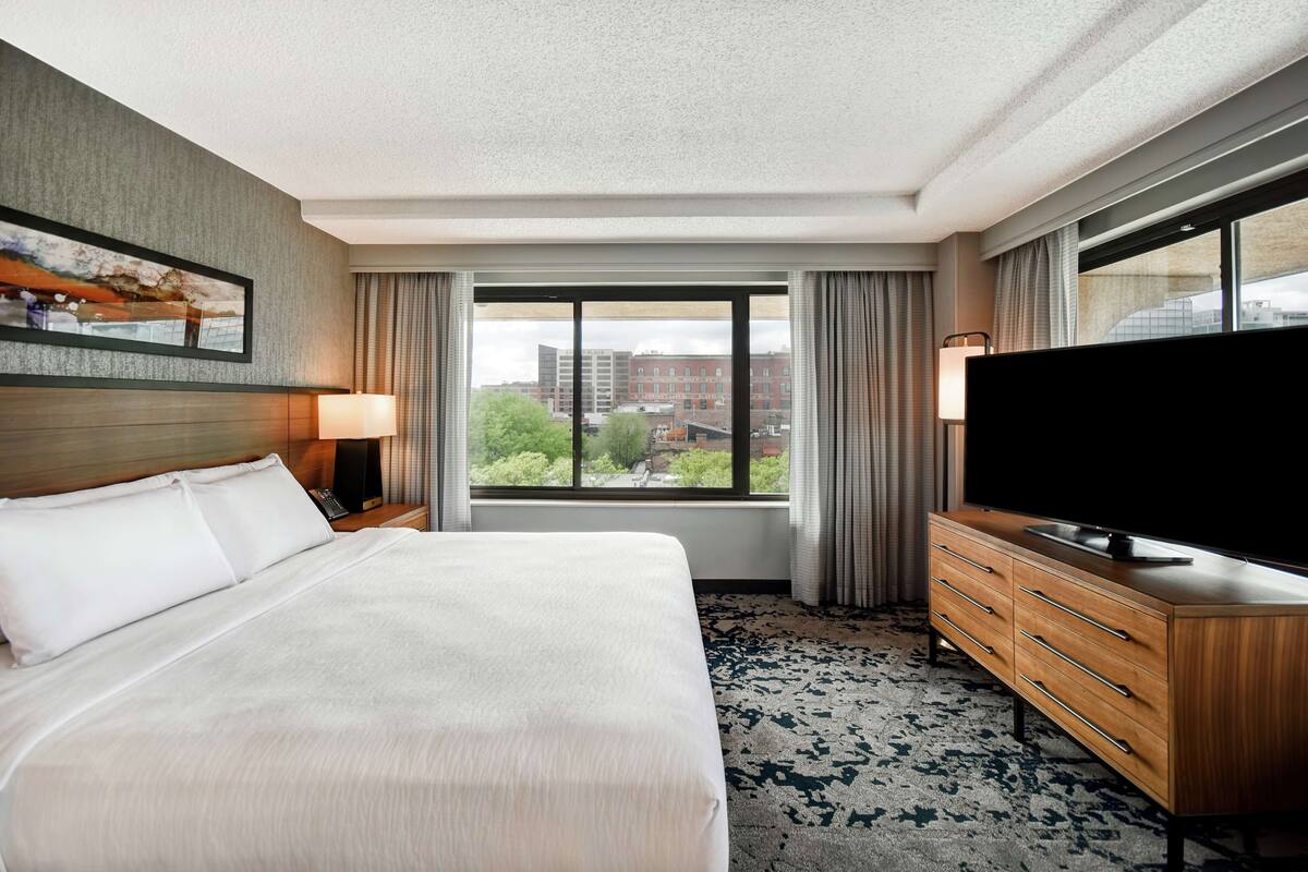 A hotel room with a large bed, a TV on a wooden dresser, and a window with curtains.