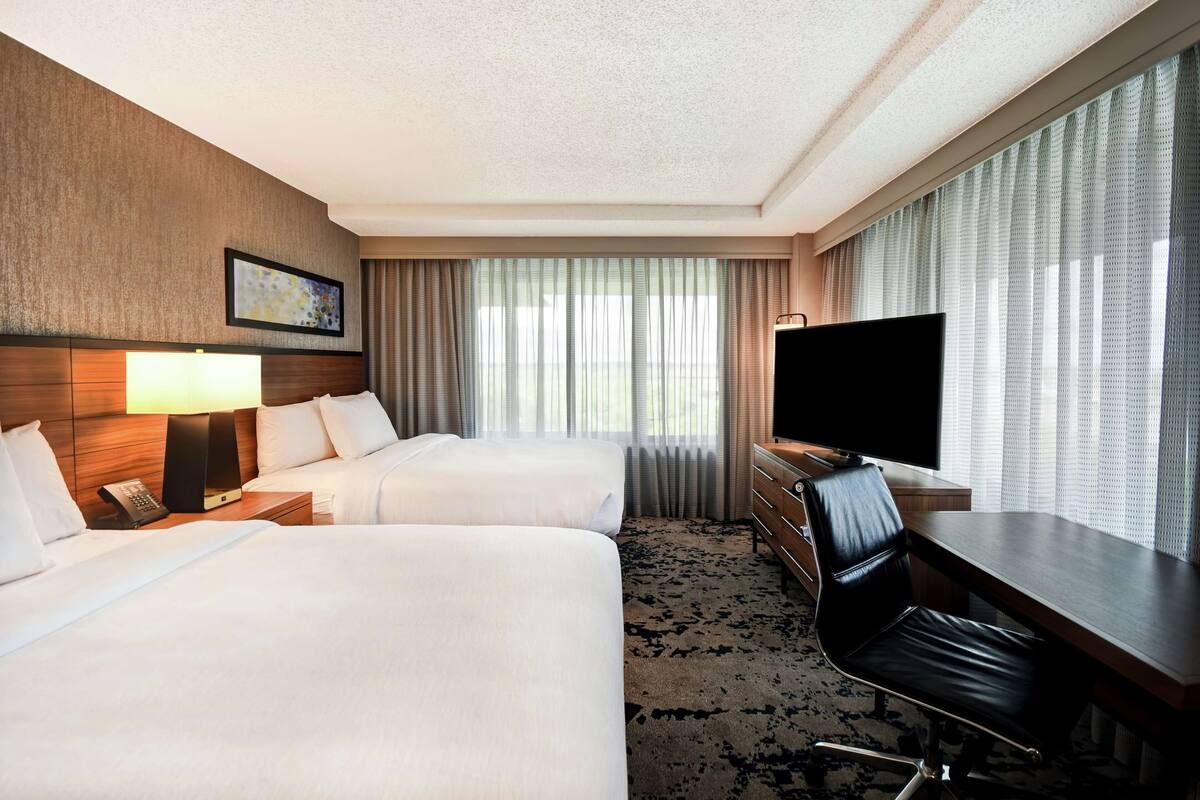A hotel room with two beds, a desk with a chair, a TV, and a painting on the wall.