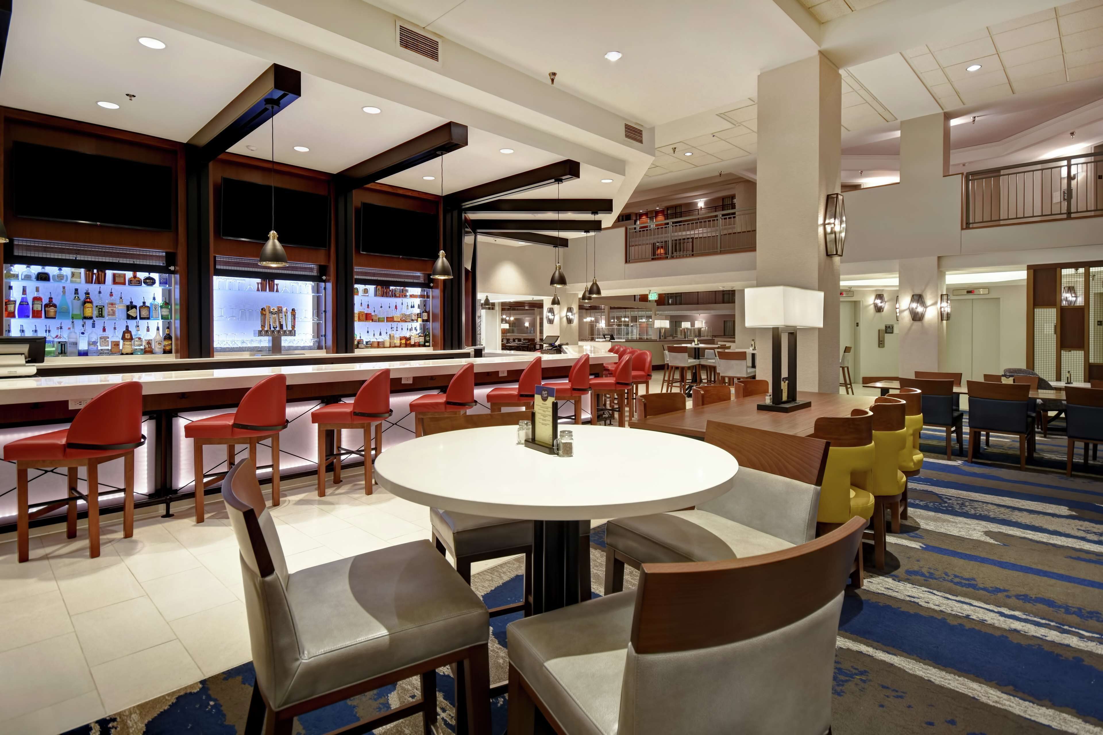 A hotel lobby with a bar area, round tables, and red and yellow chairs.