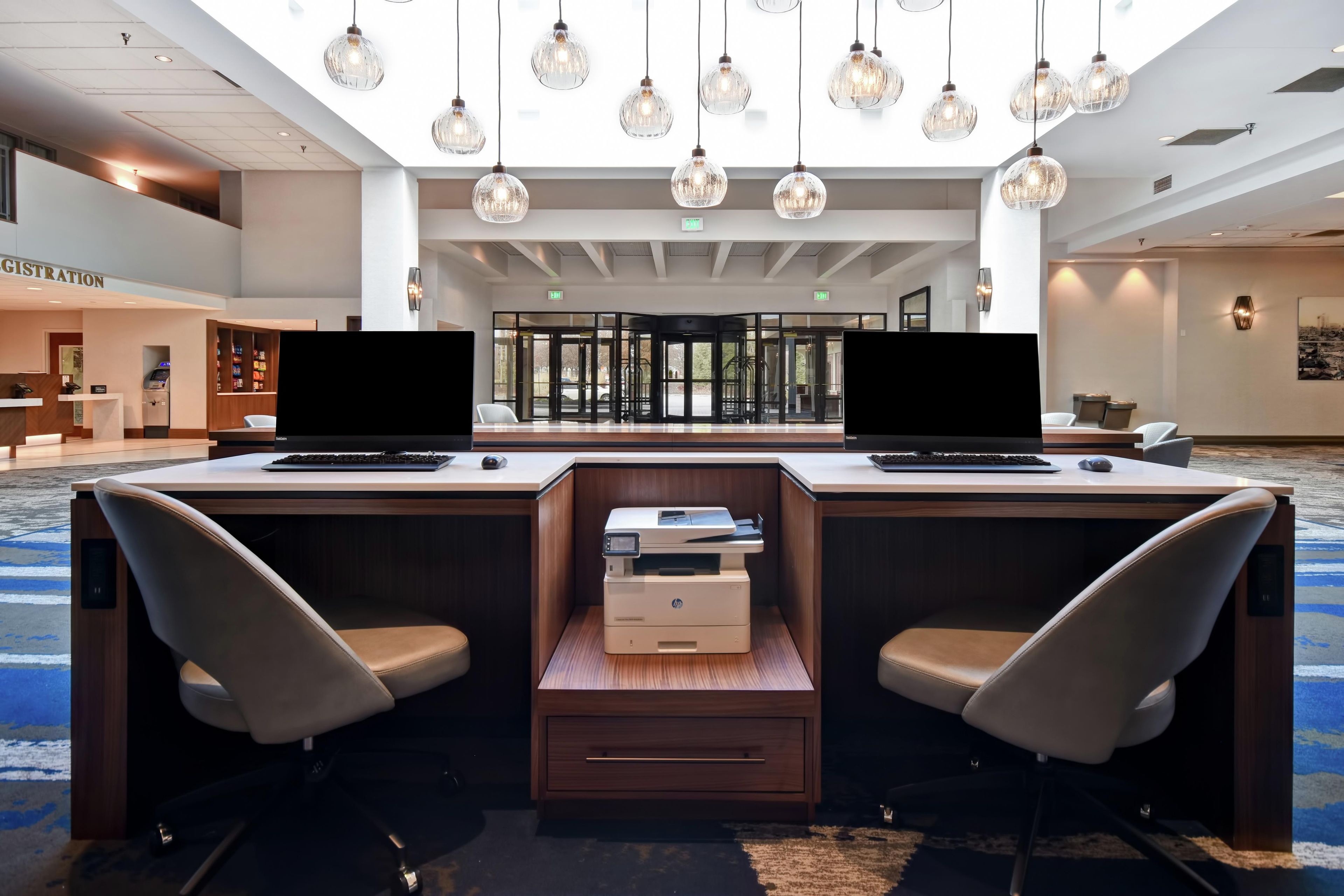 Ein Hotelrezeptionstresen mit zwei Computern, einem Drucker und einem sich drehenden Eingang.