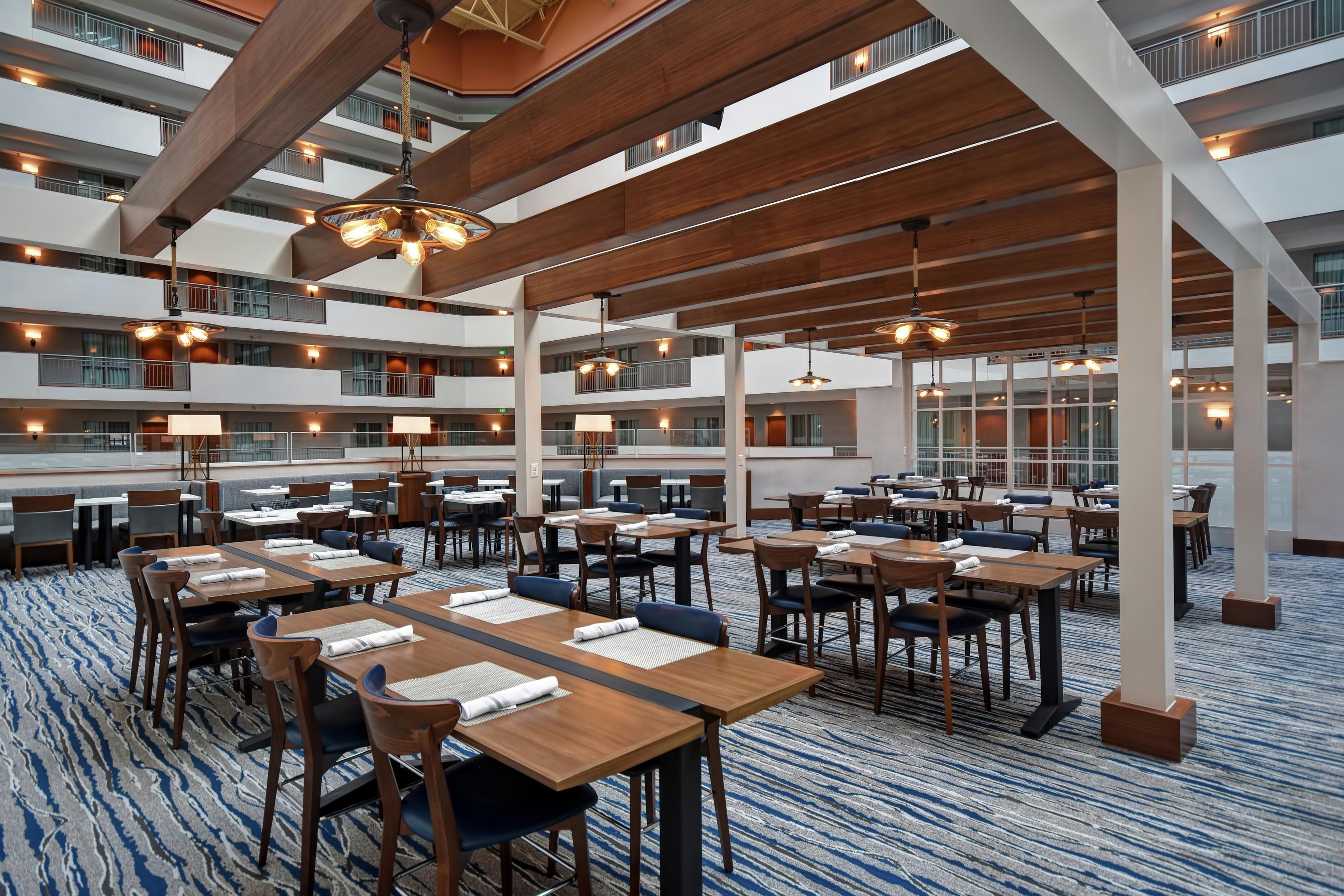 A hotel lobby with multiple dining areas, wooden ceiling beams, and a high ceiling.