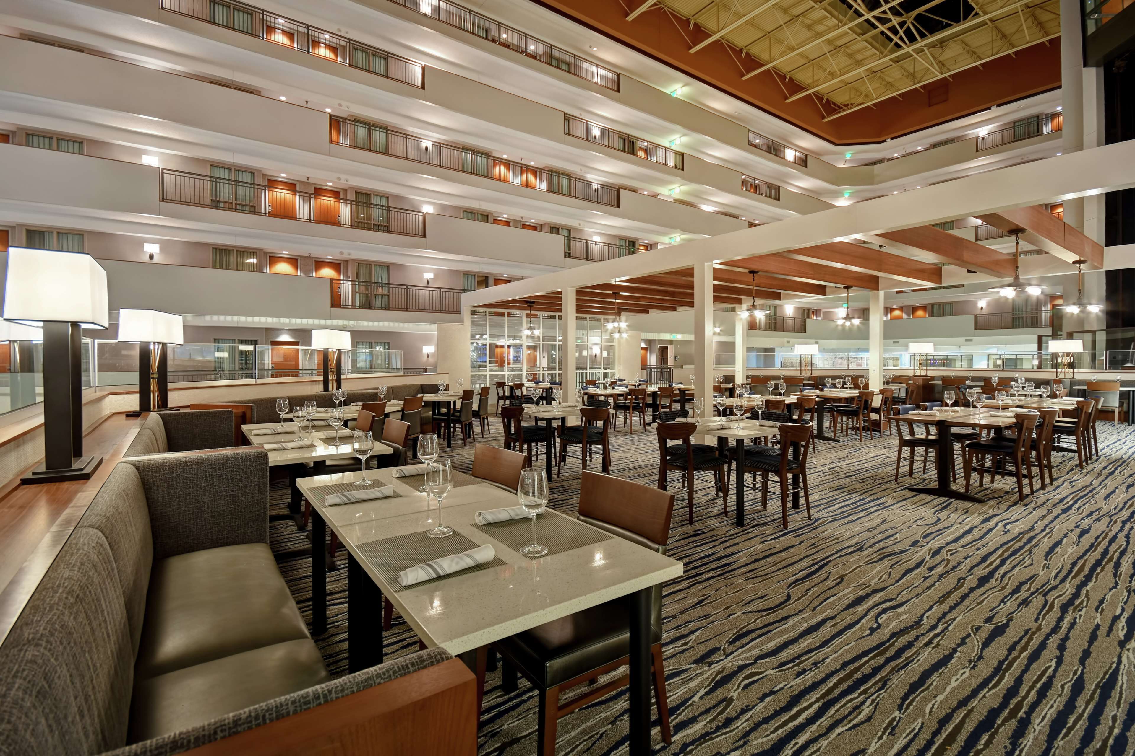 Un amplio hall de hotel con varias zonas de restauración, asientos cómodos y un techo alto con vigas a la vista.